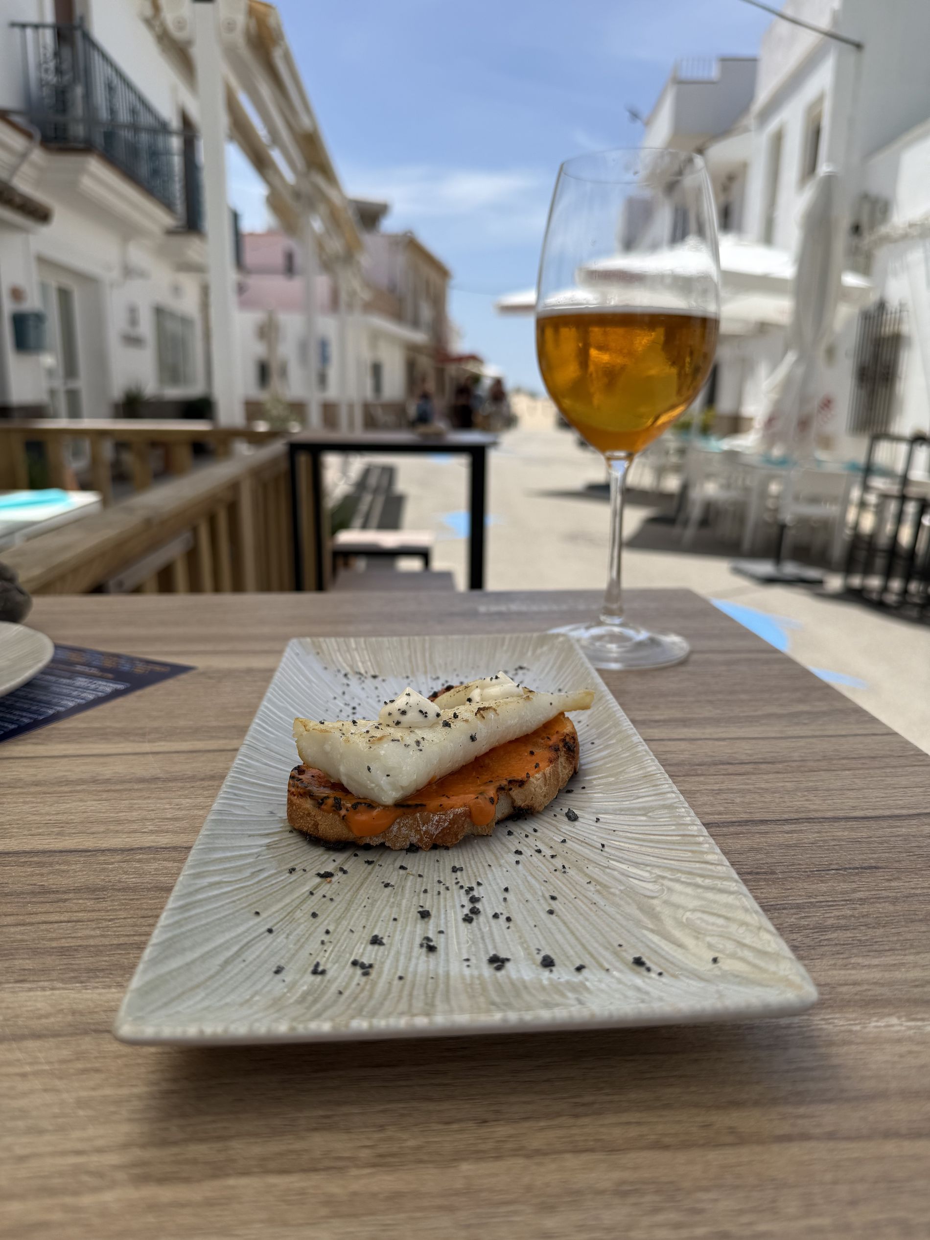 Terraza de Barlovento con una tosta de atún y una caña frente a una calle de Zahara de los Atunes